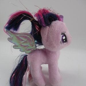 May include: A plush purple pony with a pink and blue mane and tail. The pony has iridescent wings and a purple horn.