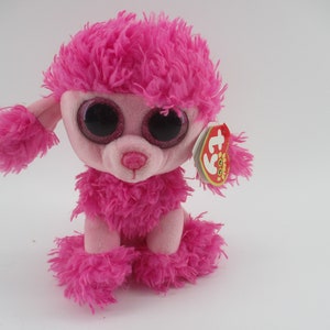 May include: A pink plush poodle toy with large, glittery eyes and a pink nose. The poodle has fluffy, textured fur in a vibrant pink color. A red and yellow tag is attached to the ear.