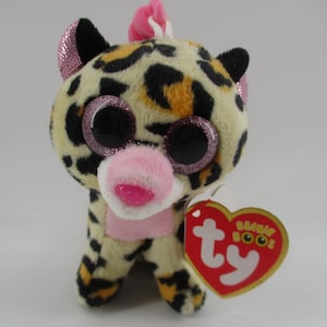 May include: A small plush leopard with pink glitter on its ears and a pink bow on its head. It has large glittery eyes and a pink nose. The plush toy is holding a red heart-shaped tag with the words "Ty Beanie Boos" on it.