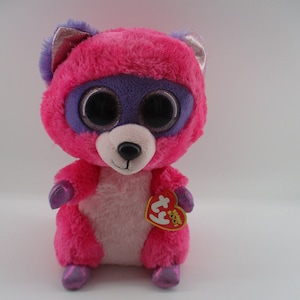 May include: Pink and purple plush raccoon with large, black eyes and a white belly. The plush toy has a Ty tag attached to its right paw.