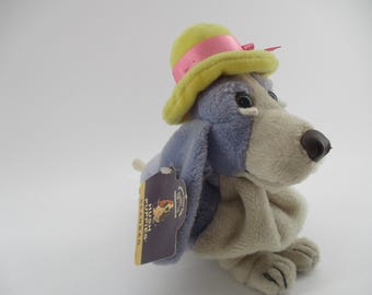 May include: A plush blue and white dog wearing a yellow hat with a pink ribbon. The dog is sitting with its head tilted to the side. The tag reads "Hush Puppies:  Wearing."