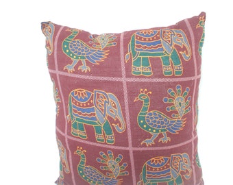 May include: A maroon pillow with a repeating pattern of elephants and peacocks. The elephants are blue, green, and yellow, and the peacocks are blue, green, and gold.