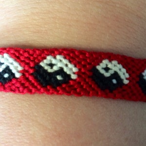 May include: Red friendship bracelet with a repeating pattern of black and white yin yang symbols.