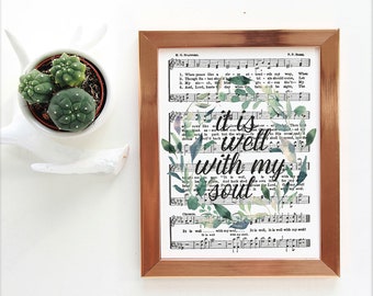 May include: A framed print with a watercolor floral wreath surrounding the text "it is well with my soul". The print is on a vintage sheet music background.
