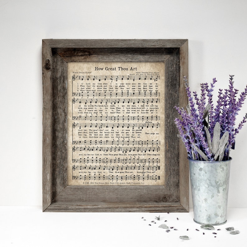 May include: A framed print of a vintage hymn sheet music with the title "How Great Thou Art". The sheet music is printed on aged paper with a brown background and black text. The print is framed in a rustic wooden frame.