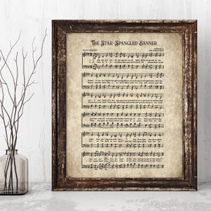 May include: A framed print of sheet music for "The Star-Spangled Banner" in a dark brown wooden frame. The sheet music has a vintage, aged appearance with musical notes and lyrics.