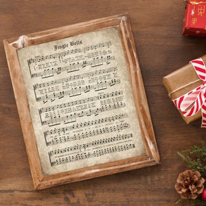 May include: A vintage-style framed print of the Christmas carol "Jingle Bells" with sheet music and lyrics. The print is on a light brown wooden surface.