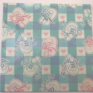 May include: A light blue and white checkered wrapping paper with a pattern of pink and blue baby shoes. The shoes have laces and are tied with ribbons. There are also small pink hearts scattered throughout the pattern.