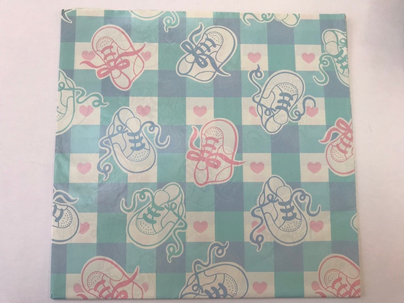 May include: A light blue and white checkered wrapping paper with a pattern of pink and blue baby shoes. The shoes have laces and are tied with ribbons. There are also small pink hearts scattered throughout the pattern.