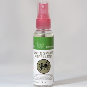May include: A clear plastic bottle with a pink spray top and a green and white label. The label says "Ant & Spider Repellent" and has a picture of an ant and a spider with a red slash through them. The bottle is 2 oz.