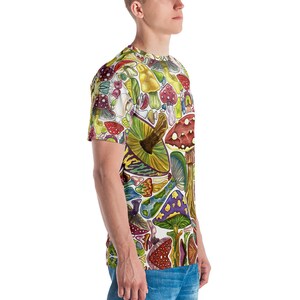 K&ouml;nnte beinhalten: Ein wei&szlig;es T-Shirt mit einem bunten Allover-Druck aus verschiedenen Pilzen. Die Pilze sind in verschiedenen Formen, Gr&ouml;&szlig;en und Farben, darunter Rot, Gelb, Gr&uuml;n, Lila und Braun.