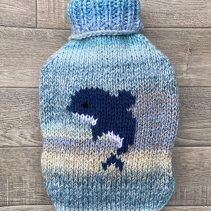 May include: A blue and beige knitted hot water bottle cover with a blue whale design.