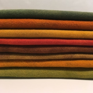 May include: A stack of ten fabric squares in various shades of green, orange, brown, and yellow. The fabric is a soft, textured wool.
