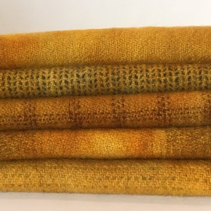 May include: A stack of five fabric swatches in various shades of yellow. The fabric has a woven texture and appears to be wool.