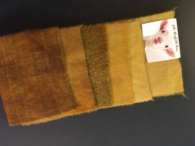 Puede incluir: Una colecci&oacute;n de muestras de tela texturizada en tonos marrones y amarillos, dispuestas en fila. Una peque&ntilde;a tarjeta con la imagen de un cordero y el texto "Julie Mayfield Moore" est&aacute; adherida a la tela.