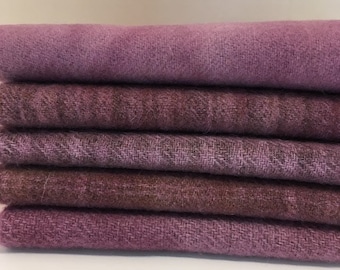 May include: A stack of six folded fabric pieces in shades of purple and mauve. The fabrics have a textured appearance, with visible woven patterns. The colors range from light lavender to deep plum.