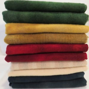 May include: A stack of 10 fabric squares in various colors, including green, yellow, red, cream, and navy blue. The fabric squares are folded and stacked neatly.