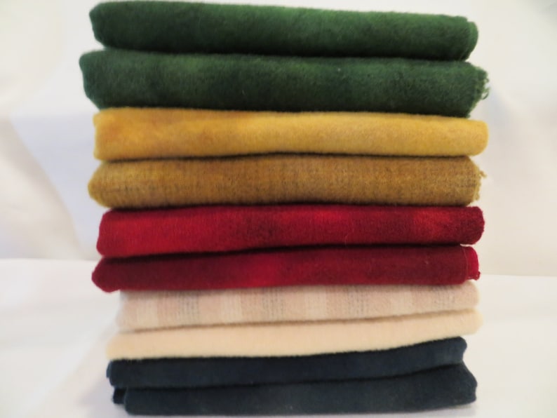 May include: A stack of 10 fabric squares in various colours, including green, yellow, red, cream, and navy blue. The fabric squares are folded and stacked neatly.