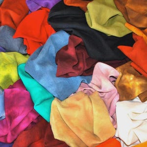 May include: A vibrant assortment of colorful suede leather scraps in various shades, including red, orange, blue, green, yellow, and purple. The pieces are piled together, showcasing the texture and diversity of the material.
