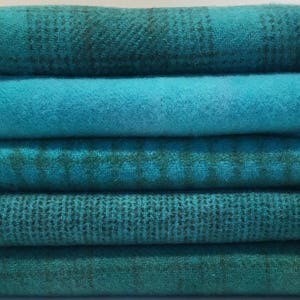 May include: A stack of six teal fabric scraps with different patterns and textures. The fabric is soft and has a slightly fuzzy texture.