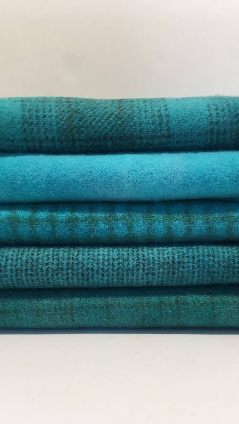 May include: A stack of six teal fabric scraps with different patterns and textures. The fabric is soft and has a slightly fuzzy texture.