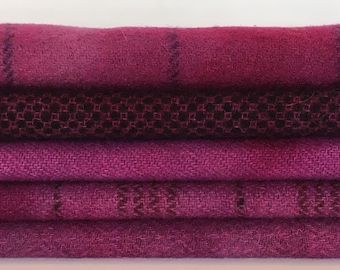 May include: A stack of four purple fabric swatches with different textures and patterns. The top swatch is a solid purple, the second is a black and purple plaid, the third is a solid purple, and the bottom is a black and purple plaid.