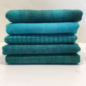 May include: Stack of six teal and green fabric squares. The fabric has a variety of textures, including plaid, woven, and solid.