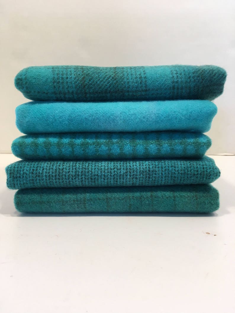 May include: Stack of six teal and green fabric squares. The fabric has a variety of textures, including plaid, woven, and solid.