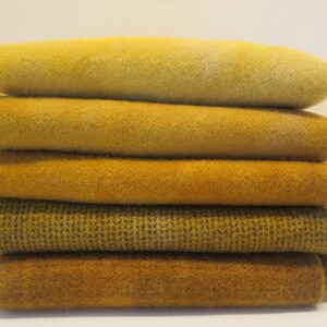 Puede incluir: Una pila de seis textiles doblados en tonos amarillos y dorados. Las telas tienen diferentes texturas, algunas lisas y otras con un patr&oacute;n tejido. Los colores var&iacute;an del amarillo p&aacute;lido a un oro profundo y rico.