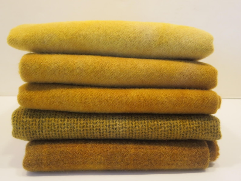 Puede incluir: Una pila de seis textiles doblados en tonos amarillos y dorados. Las telas tienen diferentes texturas, algunas lisas y otras con un patr&oacute;n tejido. Los colores var&iacute;an del amarillo p&aacute;lido a un oro profundo y rico.
