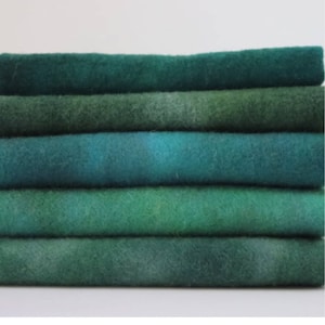 May include: A stack of six green and blue wool fabric strips. The fabric has a gradient color effect.
