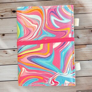 May include: A pink leather notebook cover with a colorful marbled design. The cover has two elastic bands to keep it closed.