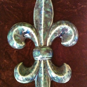 May include: A green and blue ceramic fleur-de-lis wall decor with a textured finish.