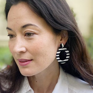 May include: A woman wearing a white button-down shirt with black and white striped hoop earrings.