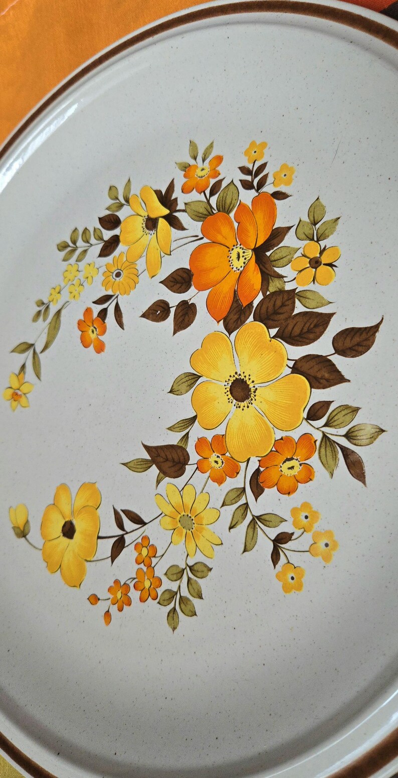 May include: Round, off-white ceramic plate with a brown rim and a floral design. The flowers are yellow and orange with brown leaves. The plate has a diameter of approximately 12 inches.