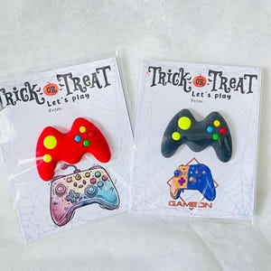 May include: Two Halloween-themed cards with controller-shaped decorations. One card features a red controller with yellow and green buttons, and a colorful controller illustration. The other card has a black controller with colorful buttons and a Game On illustration.