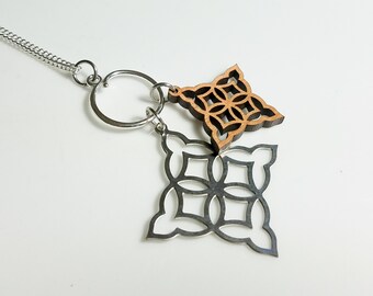 May include: A silver-toned necklace with a chain and a pendant featuring a geometric design. The pendant has two parts: a laser-cut, openwork silver shape and a smaller, wooden, four-petal flower shape.