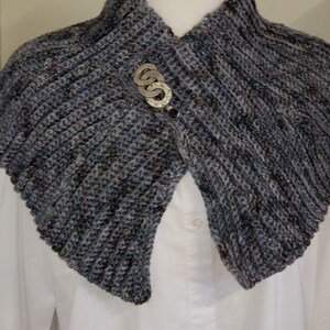 May include: A gray and blue crocheted cowl with a silver and black pin.