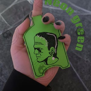 Pu&ograve; includere: Un portachiavi verde del mostro di Frankenstein. Il portachiavi presenta un contorno verde con un'immagine ricamata in bianco e nero del mostro di Frankenstein. Il portachiavi &egrave; tenuto in mano.