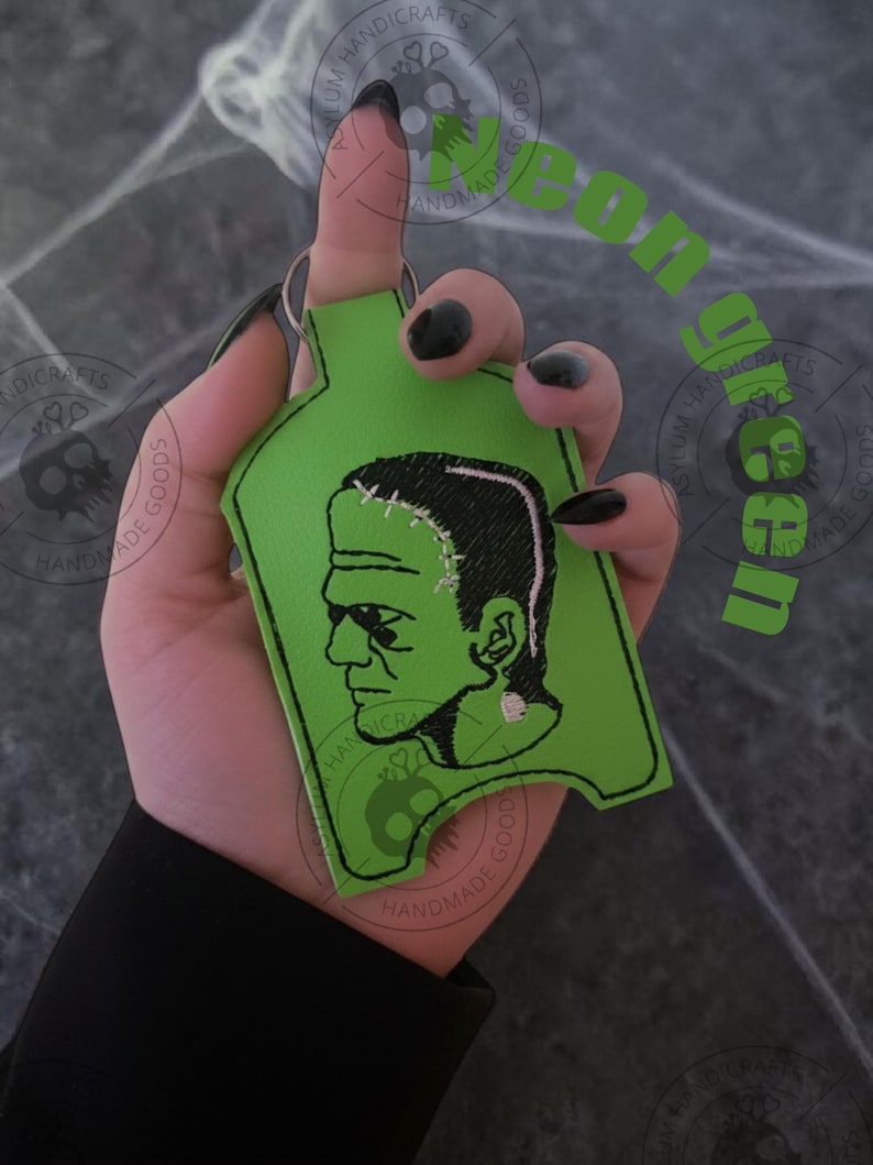 Pu&ograve; includere: Un portachiavi verde del mostro di Frankenstein. Il portachiavi presenta un contorno verde con un'immagine ricamata in bianco e nero del mostro di Frankenstein. Il portachiavi &egrave; tenuto in mano.