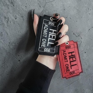May include: Black and red embroidered keychains shaped like vintage tickets. The black keychain reads "HELL ADMIT ONE 666" and the red keychain reads the same. Both have a metal ring for attaching keys.