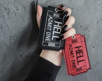 Könnte beinhalten: Zwei bestickte Schlüsselanhänger in Form von Vintage-Tickets. Einer ist schwarz mit weißem Text "HELL ADMIT ONE 666", der andere ist rot mit demselben Text. Beide haben einen Metallring für Schlüssel.