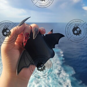 Puede incluir: Un llavero de piel sint&eacute;tica negra con forma de murci&eacute;lago y alas extendidas. El accesorio cuenta con una anilla met&aacute;lica en la parte superior. El dise&ntilde;o es de color negro s&oacute;lido con bordes cosidos, mostrando una silueta de murci&eacute;lago.