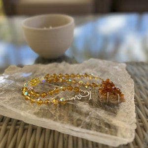 May include: A gold crystal necklace with a citrine pendant on a selenite charging plate.