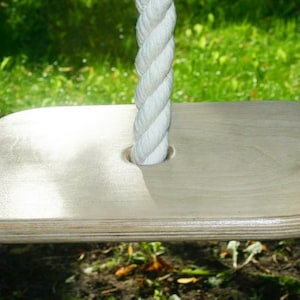 May include: A white rope swing with a wooden platform. The platform is made of plywood and has a rounded edge. The rope is thick and has a braided design.