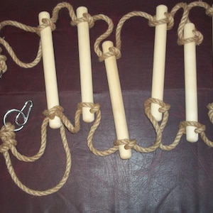 Puede incluir: Un conjunto de cinco peldaños de madera conectados por una cuerda de yute natural. La cuerda tiene dos clips metálicos en los extremos.