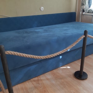 May include: A blue sofa with a rope barrier in front of it. The rope is attached to black metal posts.