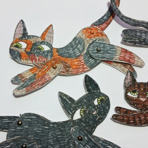 May include: Three paper cat puppets with black, brown, and orange and black markings. The puppets are made of paper and have movable limbs.