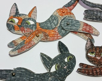 Könnte beinhalten: Drei Papier-Katzenpuppen mit schwarzen, braunen und orange-schwarzen Markierungen. Die Puppen sind aus Papier und haben bewegliche Gliedmaßen.