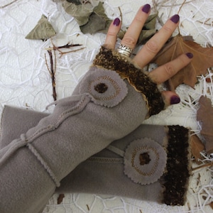 May include: A pair of gray fleece fingerless gloves with brown trim and decorative fabric flowers. The gloves have a tie at the wrist.